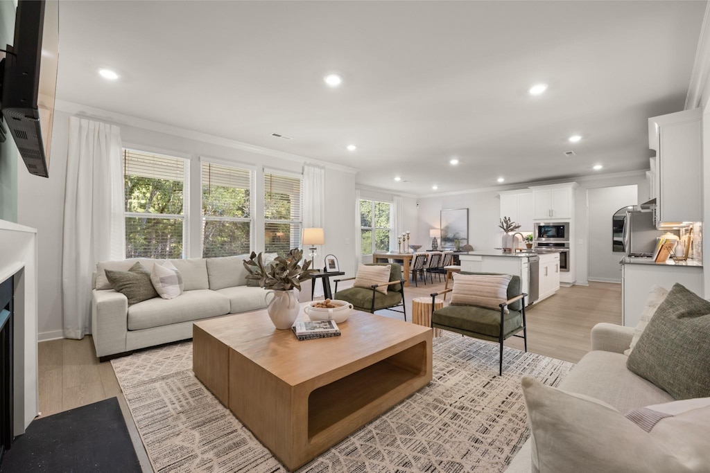 living room with ornamental molding, recessed lighting, a fireplace, and light wood-style flooring