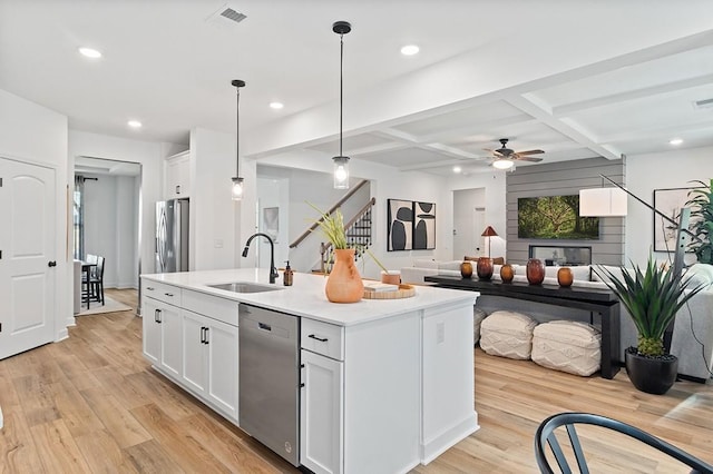 kitchen with light wood finished floors, an island with sink, coffered ceiling, stainless steel appliances, and a sink