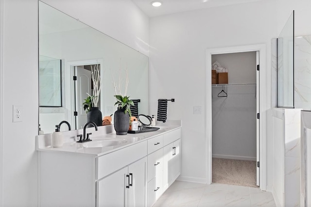 full bathroom with a walk in closet, baseboards, double vanity, marble finish floor, and a sink