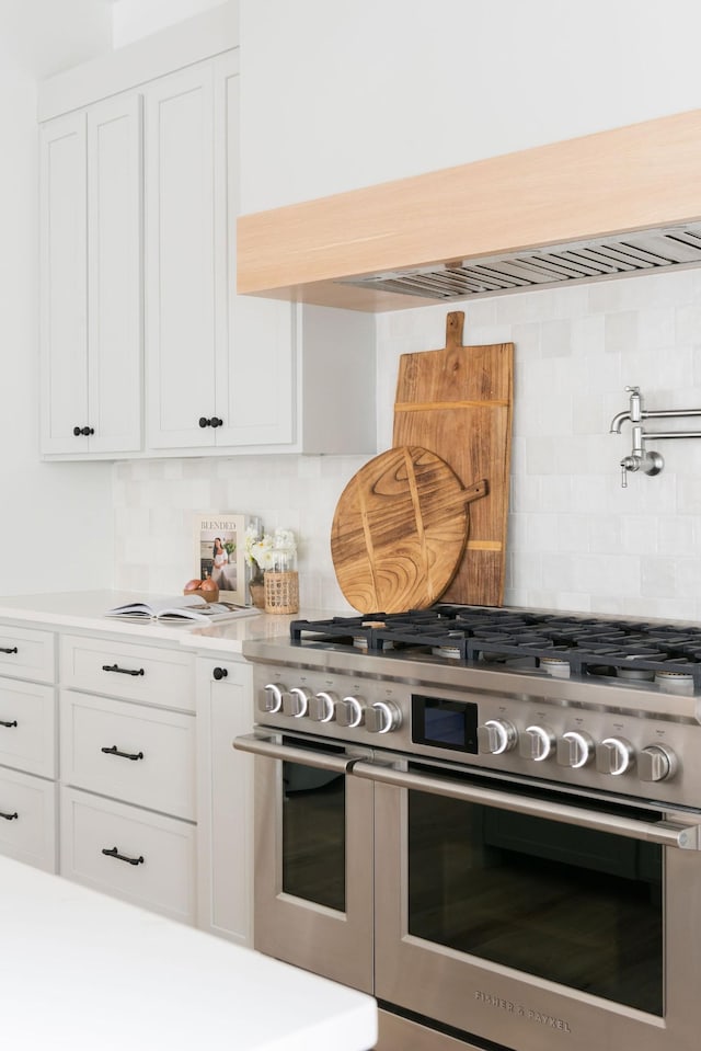 kitchen featuring white cabinetry, light countertops, double oven range, decorative backsplash, and custom range hood