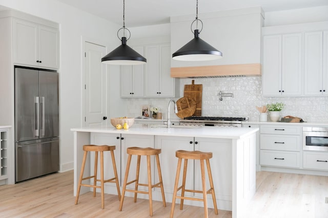 kitchen with a kitchen island with sink, a breakfast bar, white cabinetry, light countertops, and appliances with stainless steel finishes