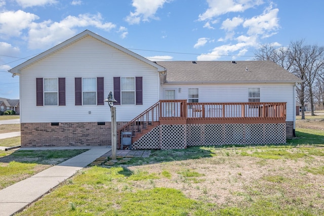 rear view of house with a shingled roof, a deck, and a yard