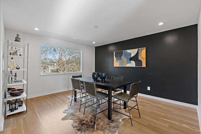 dining room featuring light wood-style flooring, an accent wall, baseboards, and visible vents