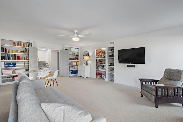 living room featuring visible vents, built in features, light colored carpet, ceiling fan, and stairs