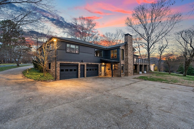 view of front of house featuring a garage, stone siding, driveway, and a chimney