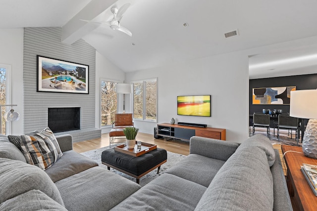 living area with vaulted ceiling with beams, a brick fireplace, visible vents, and light wood-style floors