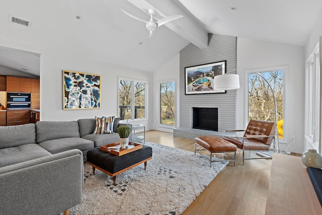 living room featuring vaulted ceiling with beams, a fireplace, a ceiling fan, visible vents, and light wood-style floors