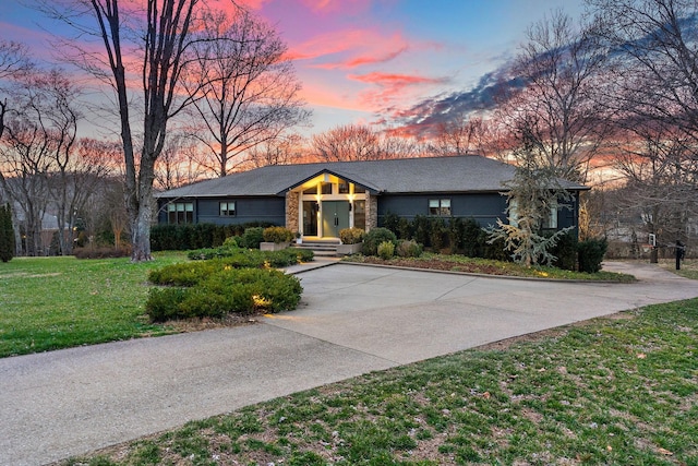 mid-century inspired home featuring driveway, a front lawn, and stone siding