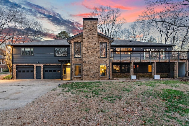 view of front facade with brick siding, a chimney, an attached garage, driveway, and a wooden deck