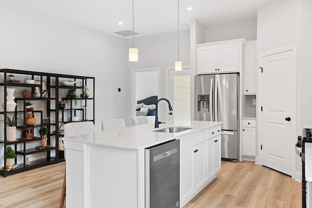 kitchen featuring an island with sink, a sink, stainless steel appliances, light wood-style floors, and light countertops