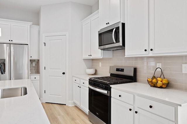 kitchen featuring stainless steel appliances, backsplash, white cabinets, and light wood finished floors