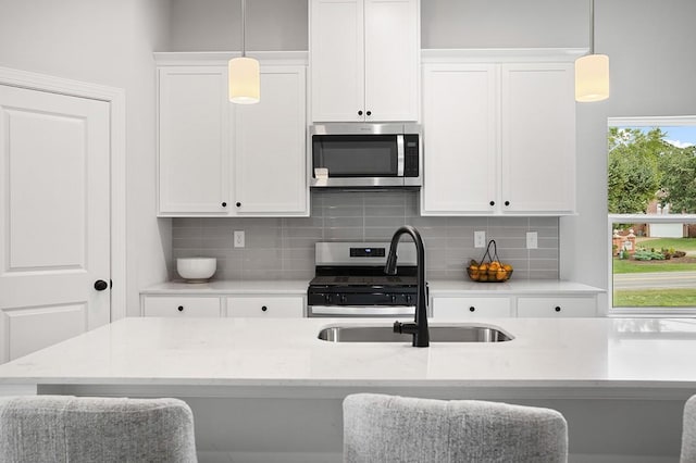 kitchen featuring decorative light fixtures, decorative backsplash, appliances with stainless steel finishes, white cabinets, and a sink