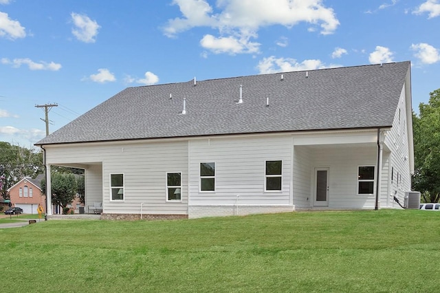 rear view of property featuring central air condition unit, a lawn, and roof with shingles