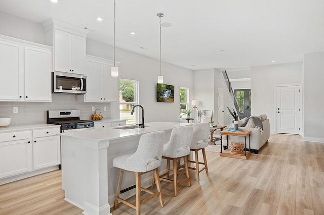 kitchen with light wood-style flooring, a kitchen island with sink, a sink, decorative backsplash, and stainless steel appliances