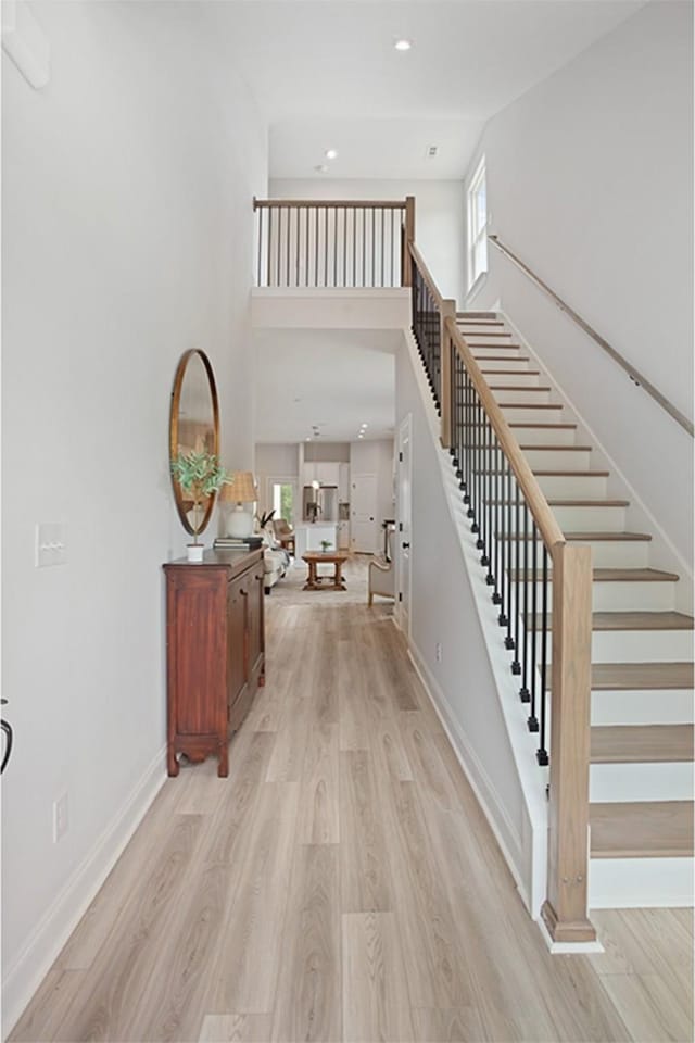 foyer entrance featuring light wood-style flooring, recessed lighting, a high ceiling, baseboards, and stairs