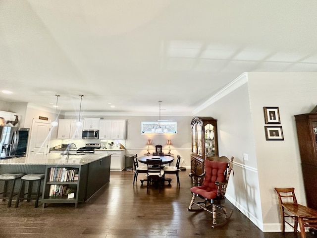 kitchen with a breakfast bar, dark wood-style flooring, white cabinets, appliances with stainless steel finishes, and an island with sink