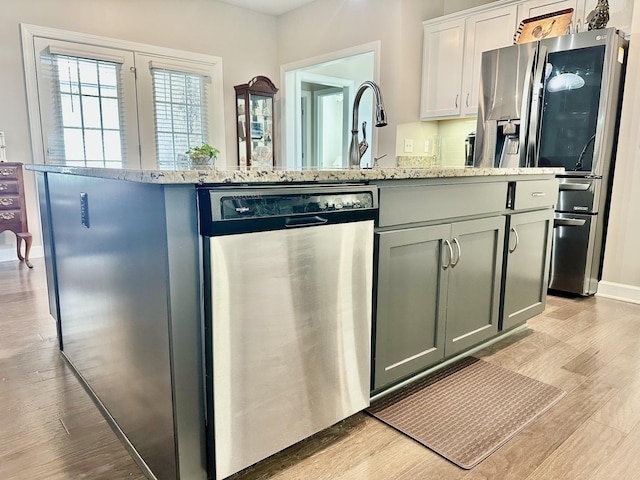 kitchen featuring light wood finished floors, a kitchen island with sink, light stone counters, and stainless steel appliances