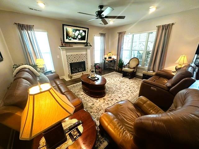 living area with a wealth of natural light, visible vents, a tiled fireplace, and wood finished floors