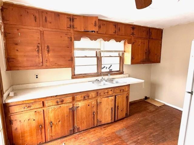 kitchen featuring dark wood finished floors, light countertops, brown cabinetry, a sink, and baseboards