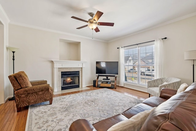 living room with ceiling fan, a fireplace with flush hearth, light wood-style flooring, and crown molding