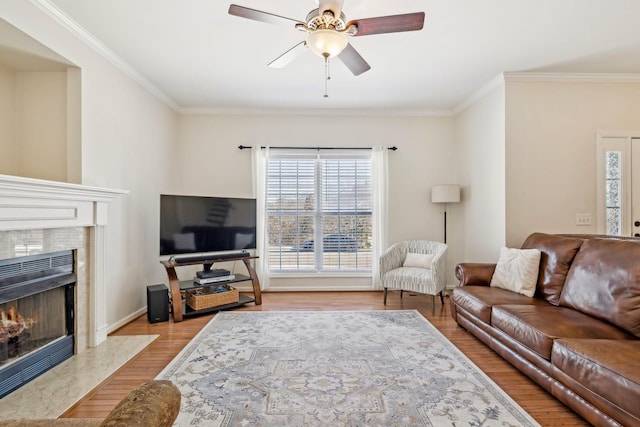 living room with light wood-type flooring, ceiling fan, a premium fireplace, and crown molding