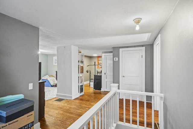 hallway featuring wood finished floors, an upstairs landing, and baseboards