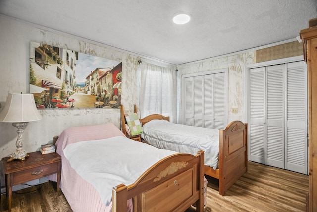 bedroom with multiple closets, wood finished floors, a textured ceiling, and wallpapered walls