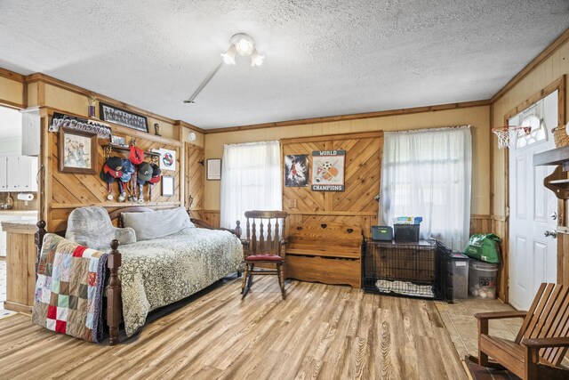 bedroom featuring light wood-type flooring, wooden walls, ornamental molding, and a textured ceiling