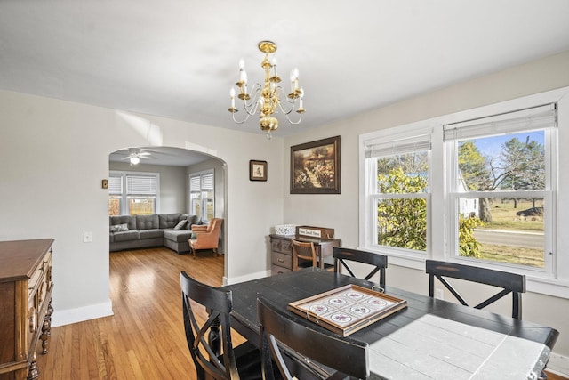 dining space with arched walkways, baseboards, a notable chandelier, and light wood-style floors