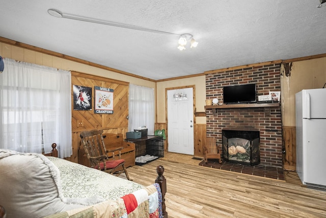 bedroom featuring ornamental molding, wood finished floors, freestanding refrigerator, a textured ceiling, and a fireplace