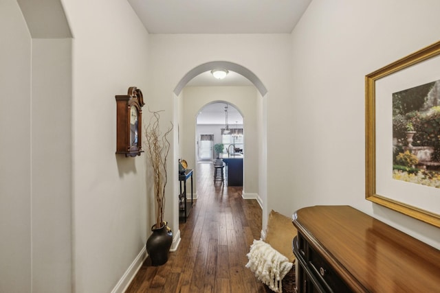 corridor featuring arched walkways, dark wood-type flooring, and baseboards