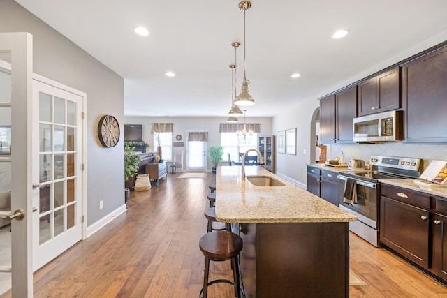 kitchen featuring a center island with sink, decorative backsplash, appliances with stainless steel finishes, light stone counters, and a sink