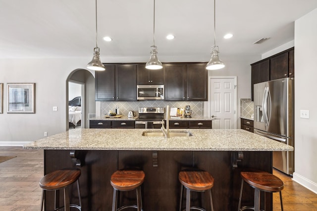 kitchen with stainless steel appliances, hanging light fixtures, a kitchen island with sink, and dark brown cabinets