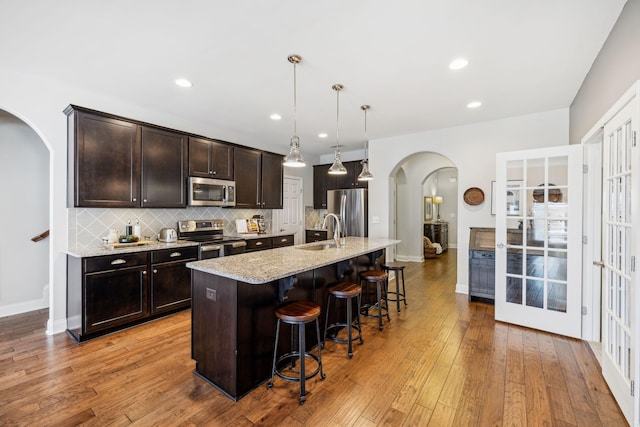 kitchen with a center island with sink, arched walkways, a breakfast bar, decorative light fixtures, and stainless steel appliances