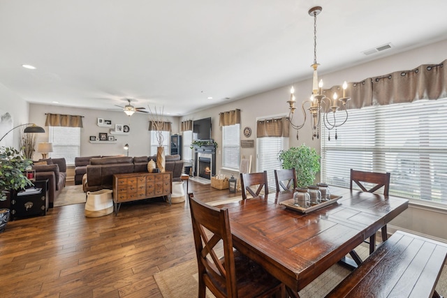 dining space featuring a warm lit fireplace, visible vents, dark wood-style floors, ceiling fan with notable chandelier, and recessed lighting