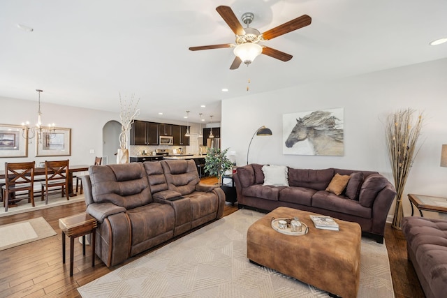 living room with arched walkways, light wood finished floors, ceiling fan with notable chandelier, and recessed lighting