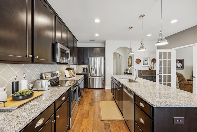 kitchen with a sink, light wood-style floors, appliances with stainless steel finishes, decorative backsplash, and an island with sink