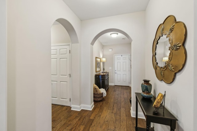 corridor with baseboards, arched walkways, and dark wood-style flooring