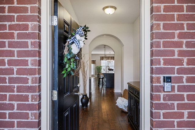 foyer with arched walkways and dark wood finished floors