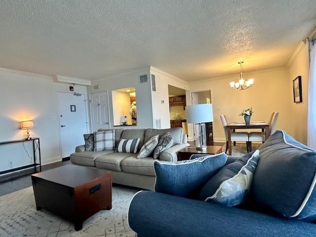 living area featuring crown molding, light wood finished floors, visible vents, a textured ceiling, and a chandelier