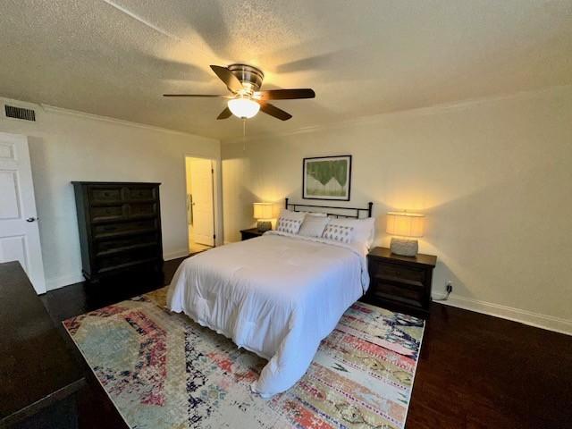 bedroom with a textured ceiling, dark wood-type flooring, visible vents, baseboards, and a ceiling fan