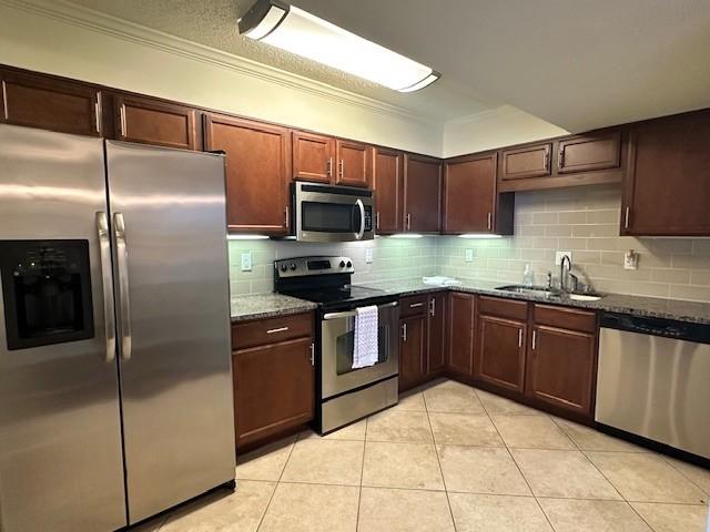 kitchen with tasteful backsplash, dark stone countertops, stainless steel appliances, a sink, and light tile patterned flooring