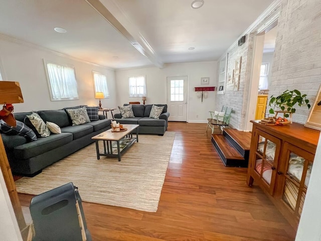 living area featuring ornamental molding, brick wall, wood finished floors, beamed ceiling, and baseboards