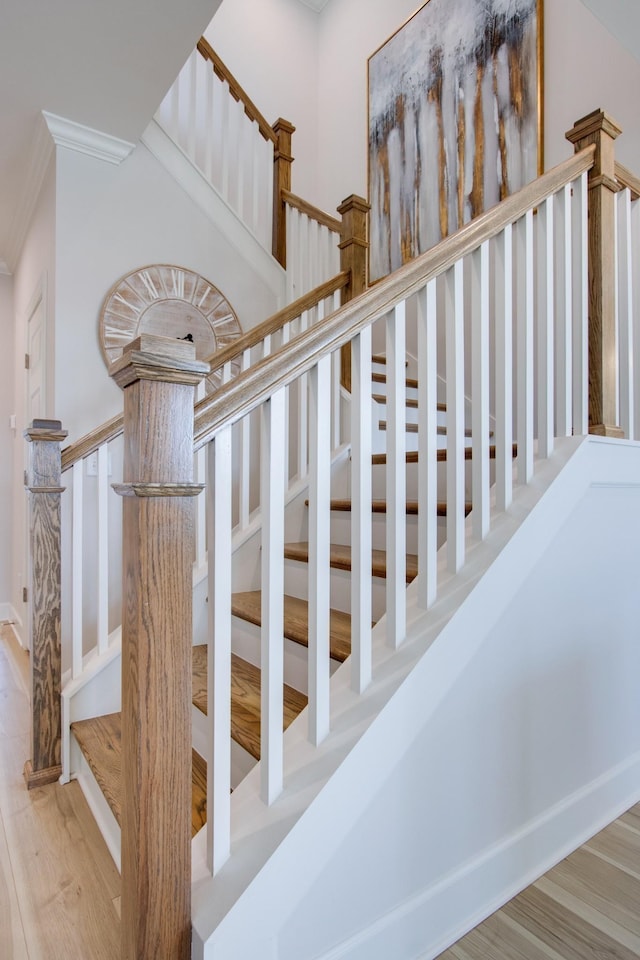 stairway with crown molding and wood finished floors