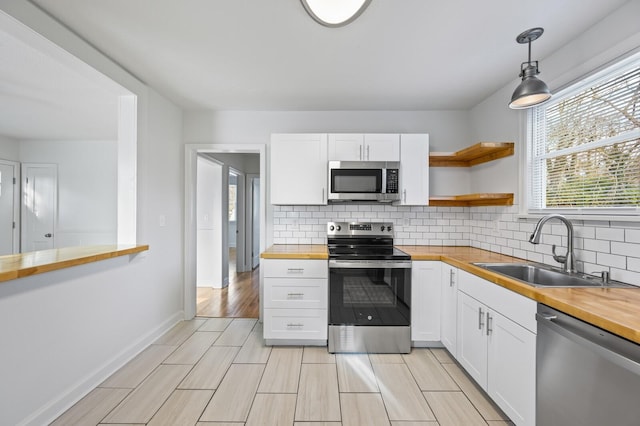 kitchen with stainless steel appliances, butcher block counters, a sink, white cabinetry, and pendant lighting