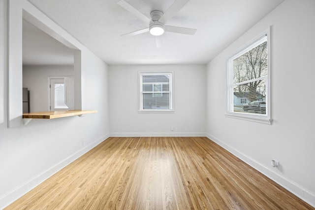 spare room with light wood finished floors, a ceiling fan, and baseboards