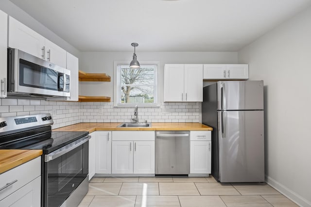 kitchen featuring a sink, wood counters, white cabinetry, appliances with stainless steel finishes, and decorative light fixtures