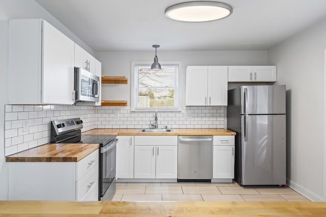 kitchen with butcher block countertops, a sink, white cabinetry, appliances with stainless steel finishes, and pendant lighting