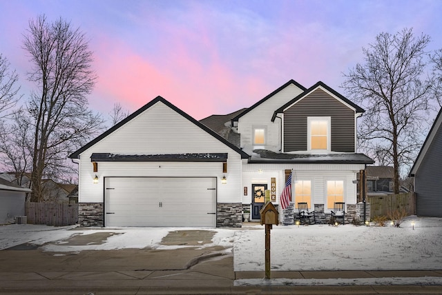 traditional home with covered porch, stone siding, an attached garage, and fence