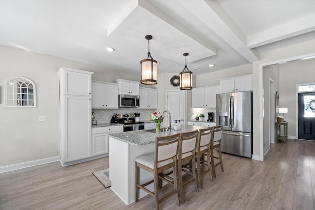 kitchen featuring stainless steel appliances, light stone counters, an island with sink, and white cabinets